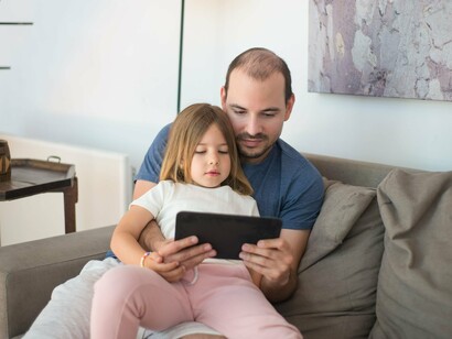 Pai e filha compartilham um momento de atenção diante de um tablet. As tecnologias digitais passaram a fazer parte das experiências cotidianas, inclusive das formas de acesso aos textos e às informações