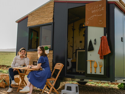 A man and a woman sitting near a black tiny portable house