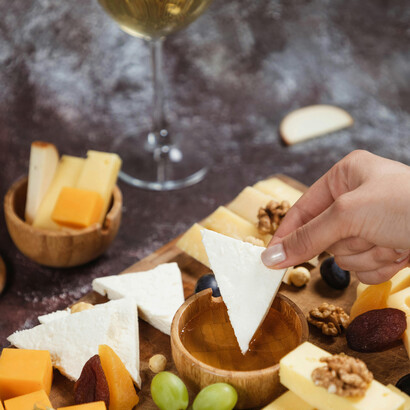 Overhead view of cheese dipped in honey, served on a rustic platter with artisanal snacks and white wine