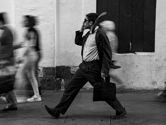 A focused man moving through a blur of rushing pedestrians, representing the modern pressure to stay constantly occupied