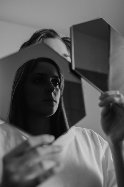 A woman holding mirrors captures her reflection within them