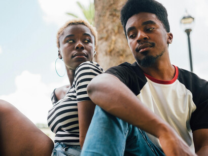 A black man and a black woman sitting down, looking at each other