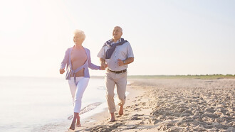 A senior couple enjoys their summer vacation, running along the beach together
