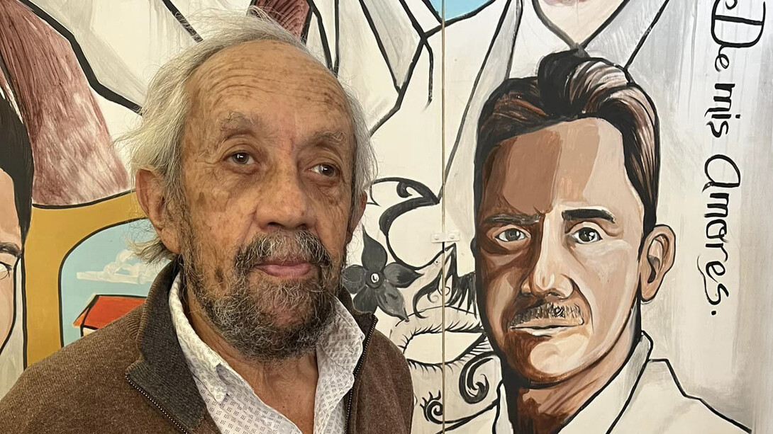 El artista Gastón González posa junto a un mural en que están representados los hombres insignes de San Felipe, Estado de México