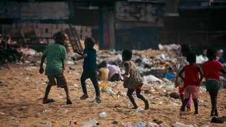 Children play on a waste-covered urban beach, highlighting the growing problem of environmental pollution
