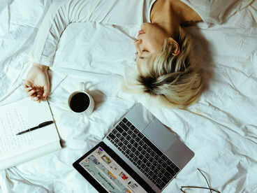 A student asleep on a bed beside a laptop and a cup of coffee, taking a break from studying