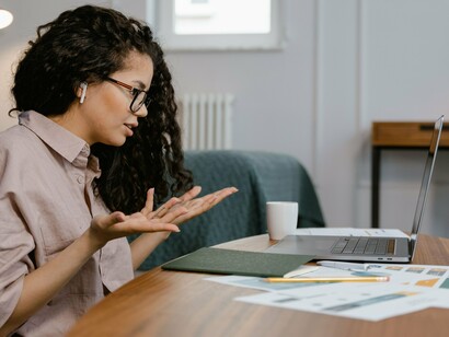 Uma mulher trabalha diante do laptop, concentrada na atividade realizada à mesa. A tela se transforma em espaço de leitura, pesquisa e produção de conhecimento, incorporando-se às práticas cotidianas de aprendizagem