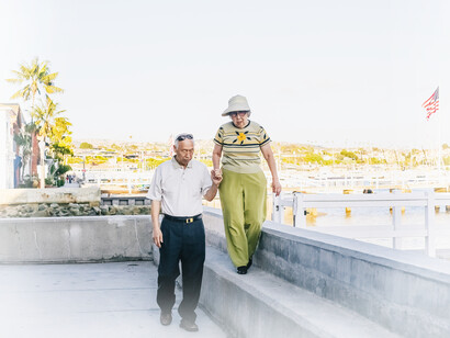 An older man and his older wife take a walk by the river