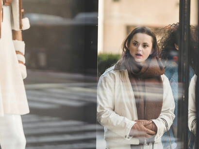 Seen through the glass, a group of cheerful, diverse women carry shopping bags past luxury store windows