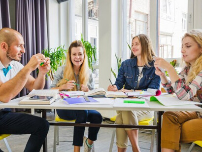 A group of young students studying together at one table, actively engaged in discussion