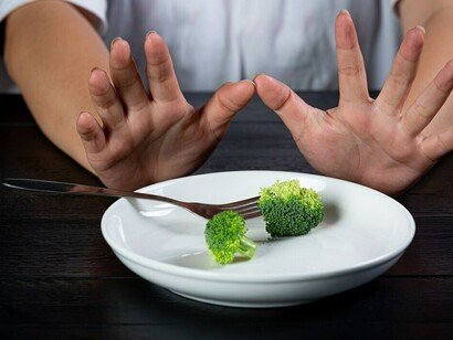 A woman refusing to eat vegetables, pushing them aside on her plate