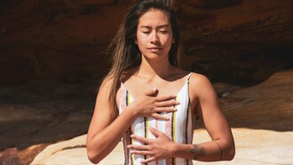 A woman practicing mindful breathing with her hands resting on her chest and abdomen, representing the calming influence of conscious breath on the nervous system