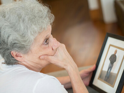 Back view of an elderly woman holding a black picture frame in a moment of grief