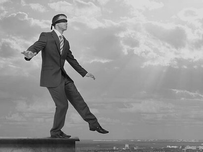 A blindfolded man standing at the edge of a cliff, symbolizing manipulation in business life