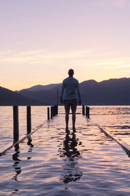 The tranquil scene of a person staring out over a body of water encapsulates the diverse philosophies on suffering, from Buddhism’s call for embracing both pleasure and pain, to Stoicism’s focus on control, and Islam’s emphasis on faith amid life's struggles