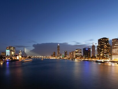 Evening blue hour in Rotterdam, with a modern bridge crossing the water and illuminated buildings reflecting across the river