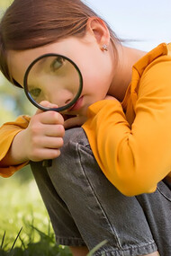 A small girl is using a magnifying glass to explore her surroundings and solve problems