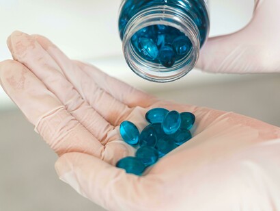 A person holds a blue pill in their hand, with a DNA strand overlay symbolizing the intersection of medicine and genetic science