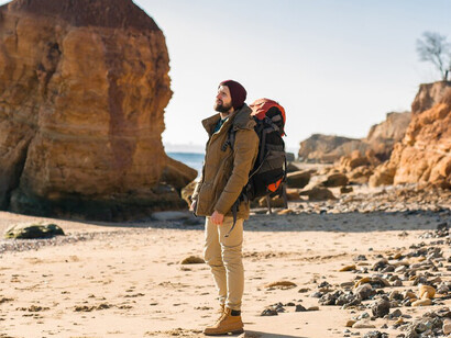 Young nomad with a backpack enjoying an autumn coastal adventure, wearing a cozy jacket and hat