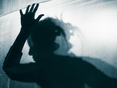 A shadowy figure leans against a translucent surface, their form distorted and blurred, highlighting the theme of alienation and disconnection