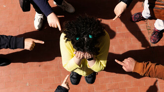 A young person wearing a garment is mocked and pointed at by classmates, experiencing bullying