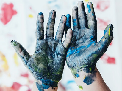 A vivid image unfolds, showcasing a child's hands adorned with blue paint, immersed in the world of arts and crafts, as they passionately paint and create