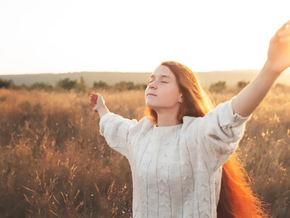 In a barren landscape, a woman stands with hands open in prayer, embodying selflessness and grace