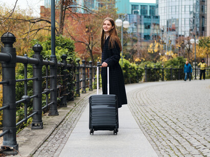 Side view of a casually dressed woman carrying a small black suitcase as she walks through the street, embodying migration, independence, and a nomadic lifestyle