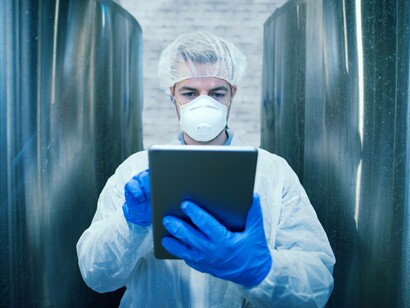 Tecnico in uniforme protettiva bianca con in mano un tablet in una fabbrica di produzione alimentare
