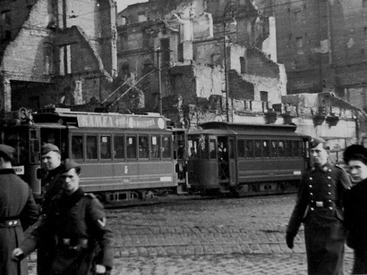 Intersection of Marszałkowska Street and Aleje Jerozolimskie during the German occupation, showing tram #3 passing by a “Kamea woda kwiatowa” billboard and the ruins of the townhouse destroyed in 1939 at Marszałkowska 98 and Aleje Jerozolimskie 33, Warsaw, Poland