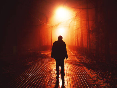 A solitary man walks through a foggy park alley at night, embodying isolation and quiet rebellion