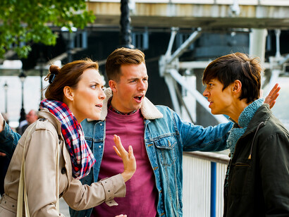 A young man steps between two people during a heated political debate, trying to prevent the argument from escalating