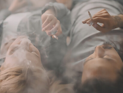 In a scene of casual rebellion, a woman and a man, donned in blue denim jeans, defy the burden of high tobacco taxes as they sit on the stairs, engrossed in their shared smoke