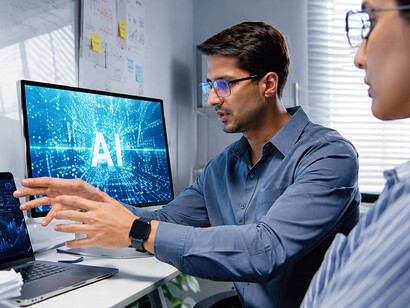 Male and female software engineers using AI-powered tools on a laptop while collaborating during a late-night meeting in a home office