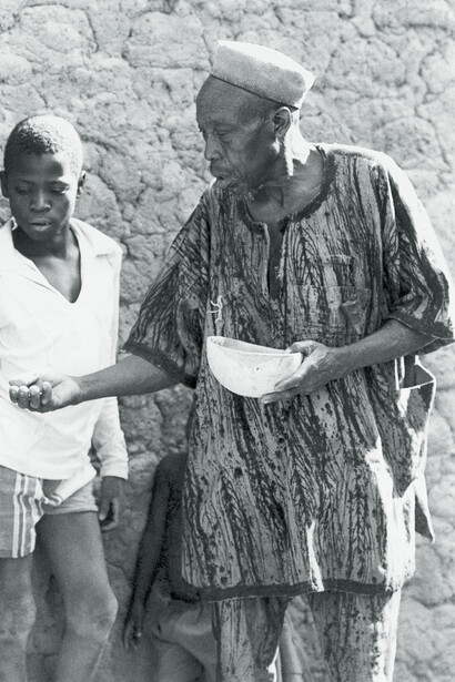 Ill. 58. Shirt with the “Nere branches” or “Nere leaves” (Nere busan, Nere furabulu) pattern. Branches are broken off the tree, the leaves stripped and the skeletal stalk dipped in mud dye before being laid onto the cotton clothing which has previously been dyed with a n’galaman solution. Unknown man, Mianka or Senari-speaking, photographed at the Nampoo-Nampon sacrifices at Sanga (not on maps), near Koutiala, 5/3/79.  
Photocredit Sarah C. Brett–Smith  
