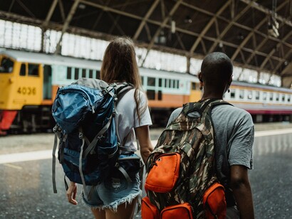 Duas viajantes caminham pela plataforma de uma estação, carregando mochilas enquanto seguem em direção ao embarque. O deslocamento começa antes de entrar no trem — e, para algumas pessoas, também é quando começam a surgir as preocupações com tudo o que pode acontecer durante a viagem
