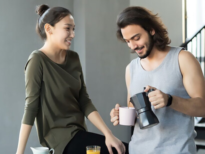 Man in gray tank top brewing coffee and pours it into a cup