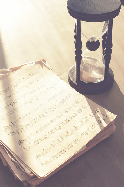 Sheets of paper with music notes are accompanied by an hourglass, blending the concepts of musical composition and the passage of time