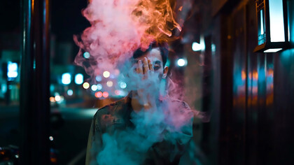 A figure, cloaked in a sleek black leather jacket, exudes an air of cool nonchalance as wisps of smoke curl around him, completing the scene with an edgy allure