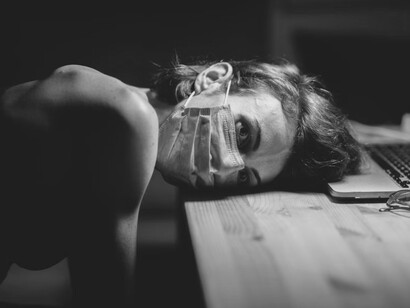 A person resting their face on a desk, covered with a mask