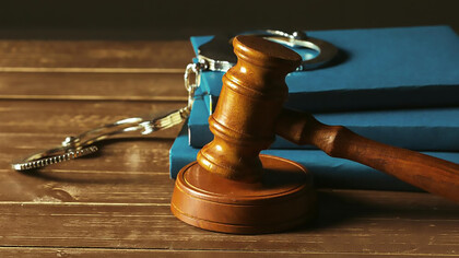 Image of a gavel resting on old wooden desk with books and manacles, representing legal system and penal reform