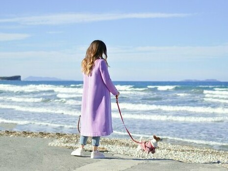 With the wind in her hair and the ocean stretching endlessly before her, a woman strolls along the beach with her loyal companion by her side and the vastness of the sea and the steady pulse of the waves that create a moment of stillness, grounding her in the present and offering a sense of perspective only nature can provide