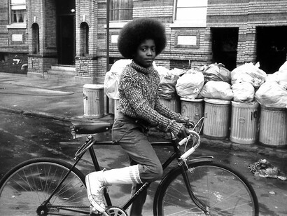 Arlene Gottfried, Boy with afro  on bicycle in front of trash cans, 1975. Courtesy of the New York Historical