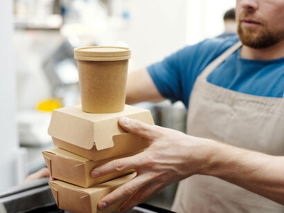 A man handing over eco-friendly food packages, featuring mycelium, coffee waste, and smart packaging solutions, showcasing the future of sustainable food delivery