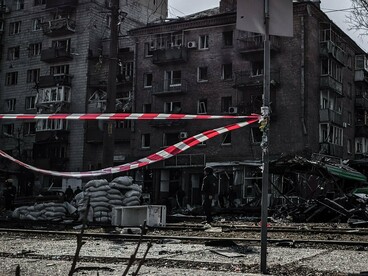 Edifícios danificados, veículos atingidos, destroços espalhados pelo chão e fitas de isolamento compõem a paisagem de uma rua de Kyiv após um ataque. A destruição da infraestrutura urbana revela uma das faces mais persistentes da guerra russo-ucraniana: mesmo longe das posições de combate, os espaços de convivência e a vida cotidiana dos civis permanecem expostos à violência