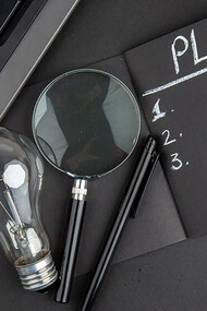 Top view of a business plan written on a black notepad with a laptop keyboard, light bulb, and pen on a black table