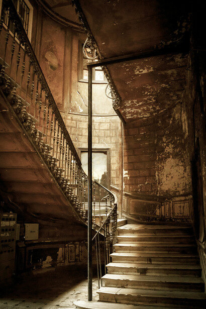 A dark, decaying interior where cracked and broken tiles lie unevenly across the floor near the stairs