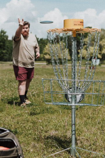 A man aims and throws a disc at the basket on a disc golf course