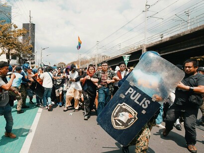 Crowds of protesters pushing against riot police, representing the growing public anger toward perceived government corruption