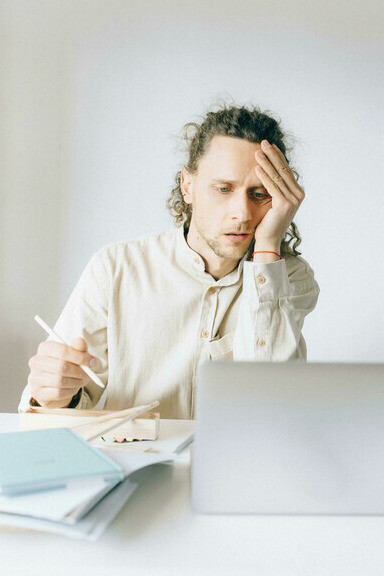 A man in a white shirt sits at a table, exhausted from work